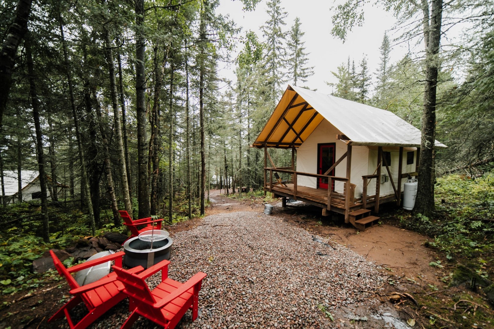 Secluded forest cabin with red chairs by lake.