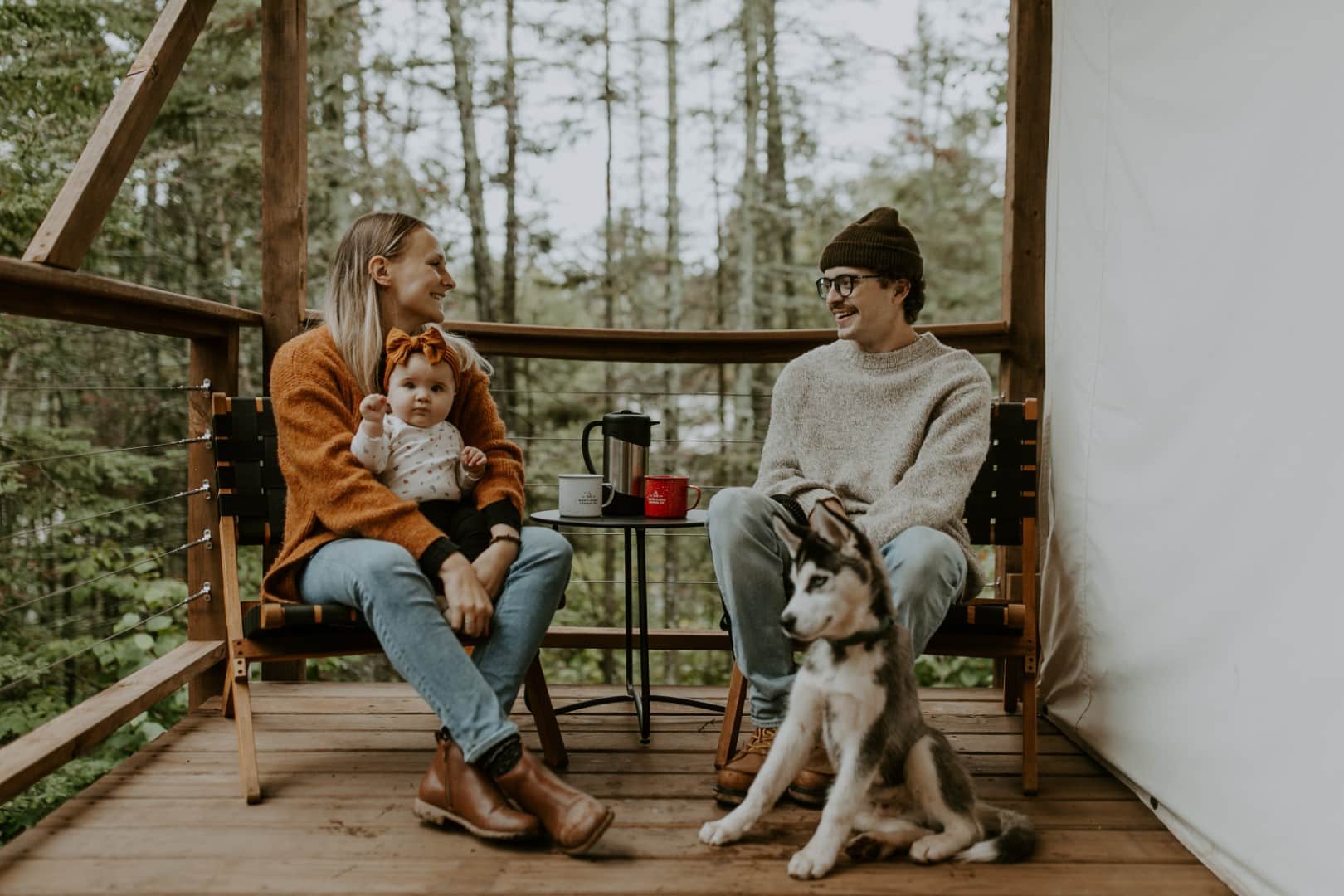 Family with baby and dog on porch in forest.