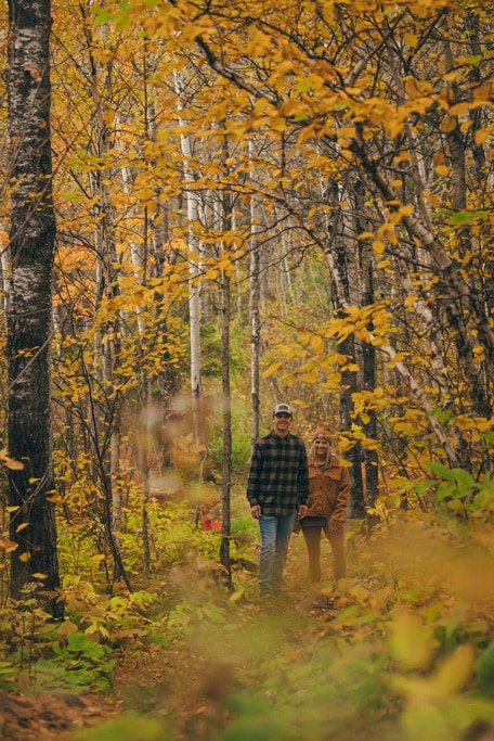 Couple walking through autumn forest with yellow leaves.