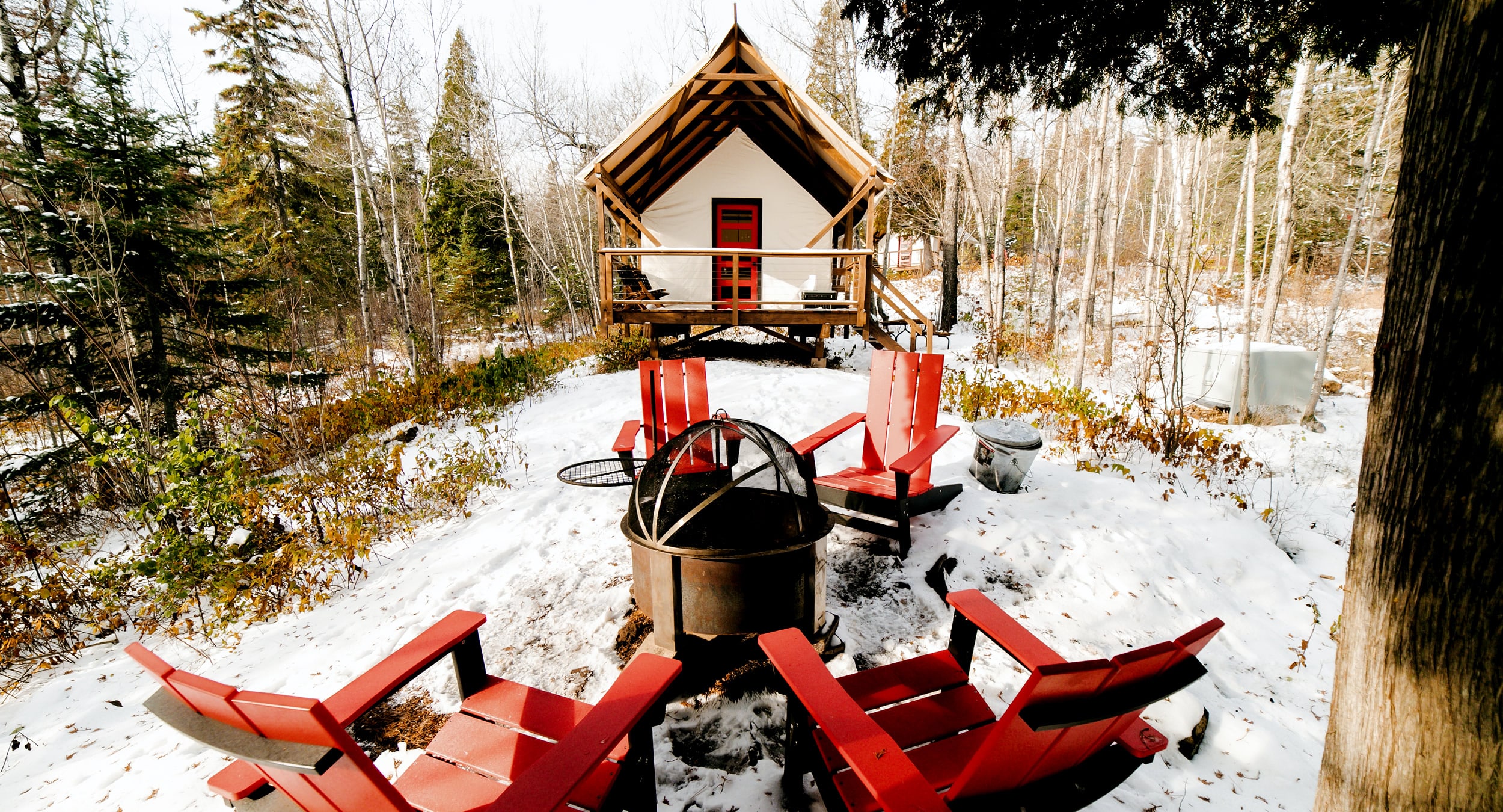 Winter cabin with fire pit and red chairs.