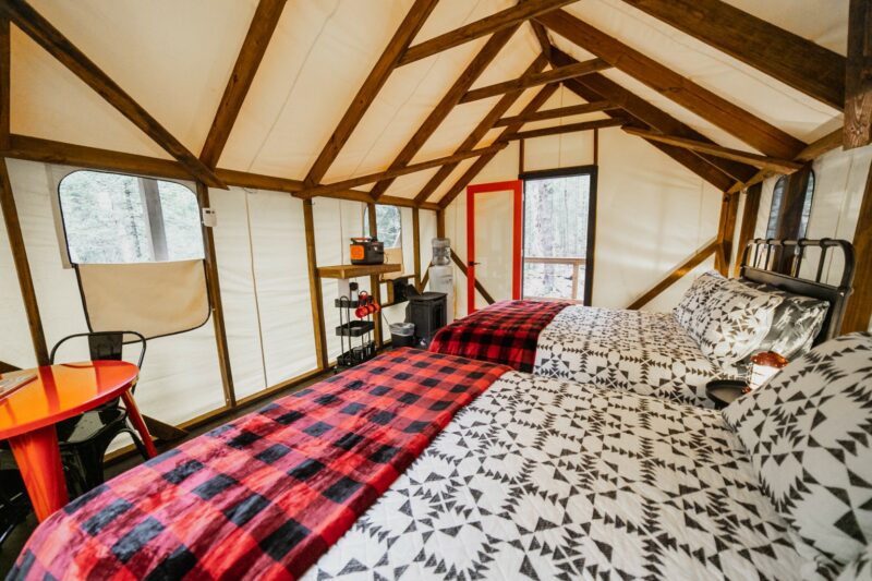 Cozy glamping tent interior with bed and wood stove.