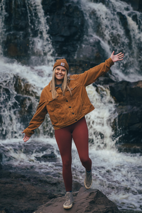 Woman posing with outstretched arms in front of waterfall.