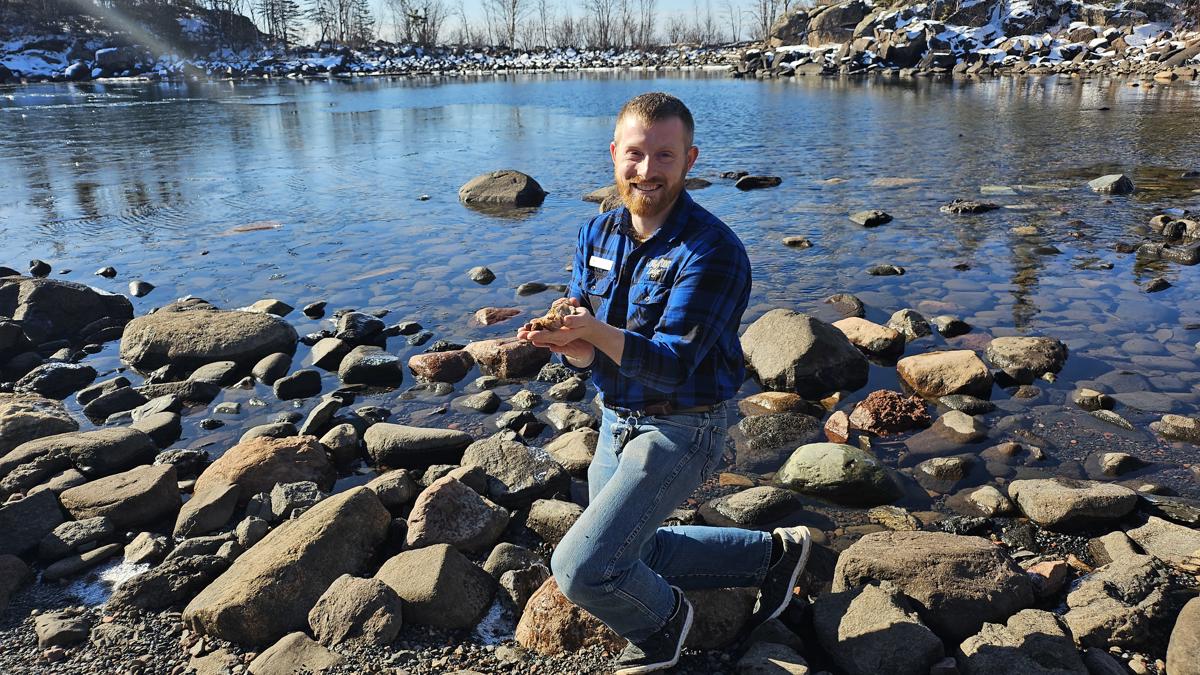 Person kneeling on rocks by a lake.