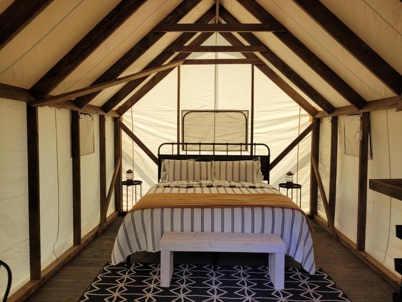 Glamping tent interior with bed and wooden beams.