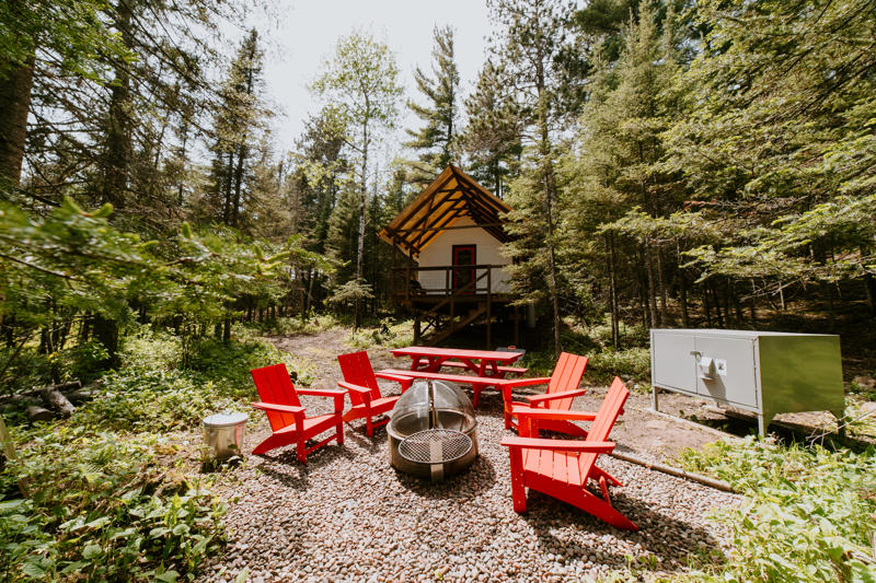 Woodland cabin with red chairs and firepit.