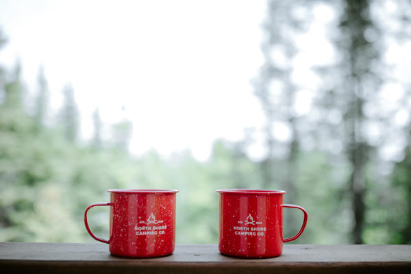 Two red camping mugs on outdoor ledge