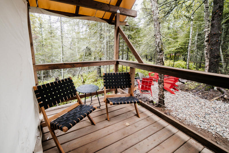 Wooden deck with chairs in forest setting.