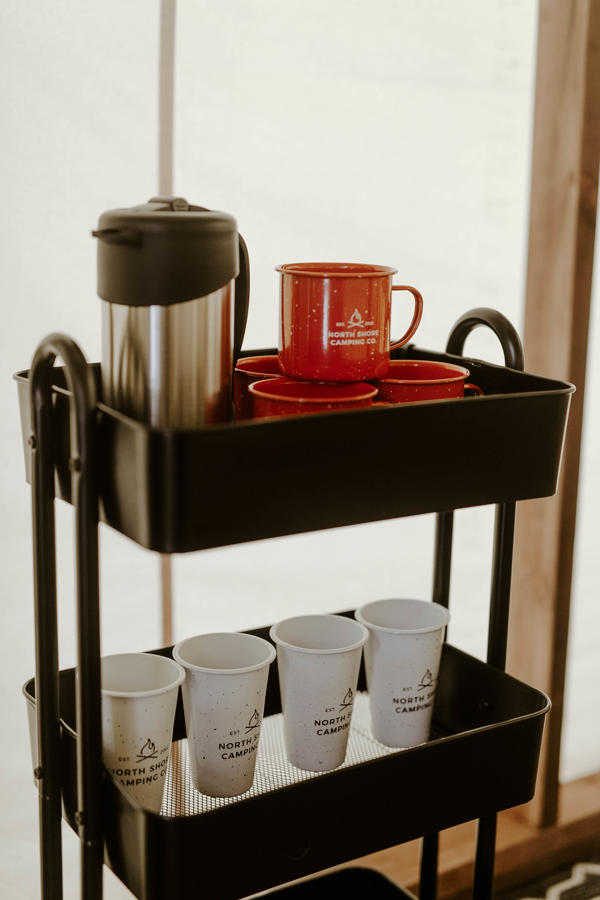 Camping mugs and thermos on a metal cart.