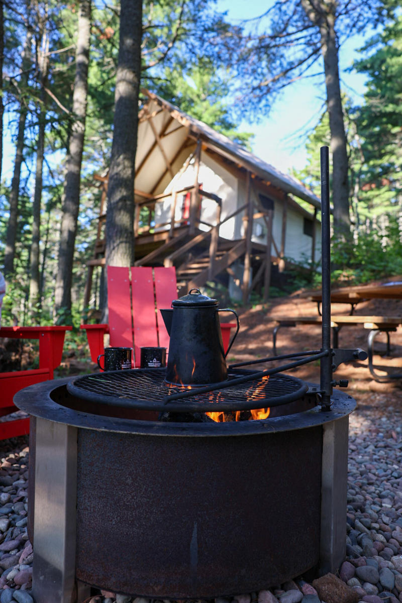 Campsite with fire pit and cabin in woods.