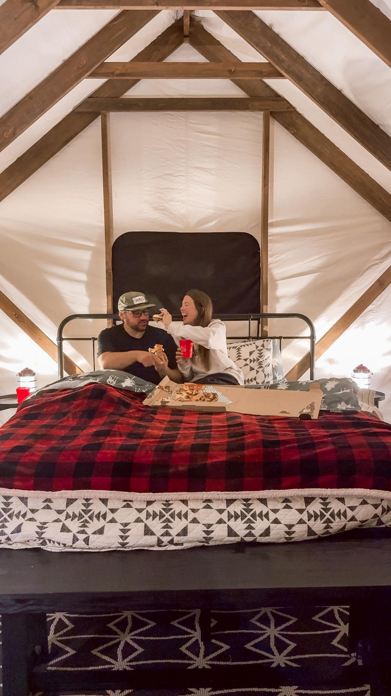 Couple eating pizza in cozy cabin bed.
