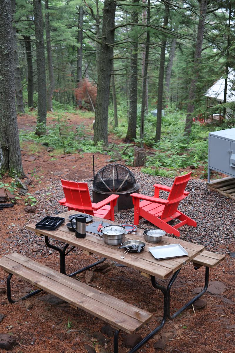 Campsite with picnic table, red chairs, and fire pit.