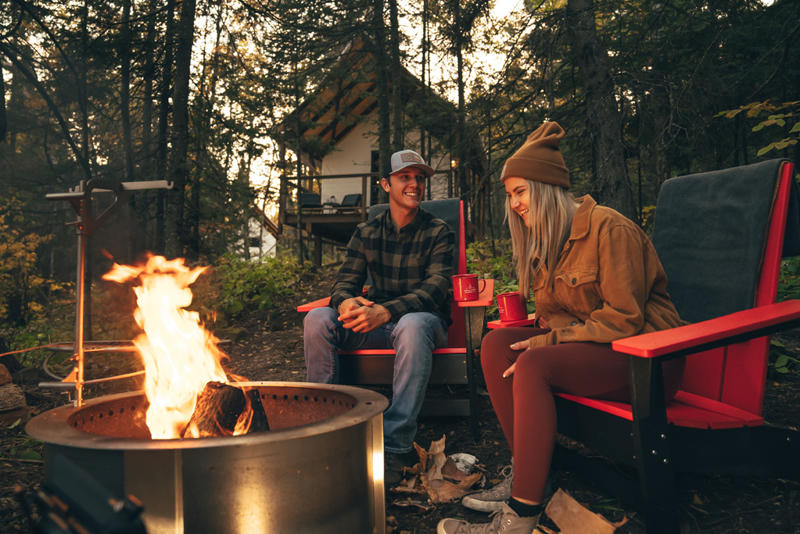 Couple enjoying campfire with mugs in forest.