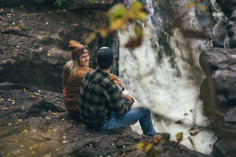 Couple sitting by waterfall in autumn forest.