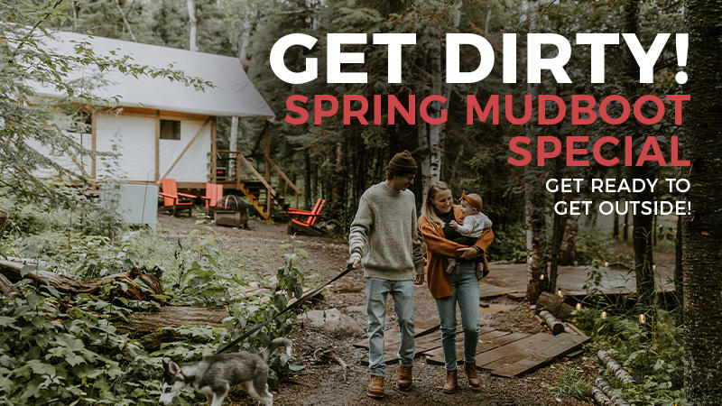 Family walks dog outside rustic cabin in forest.