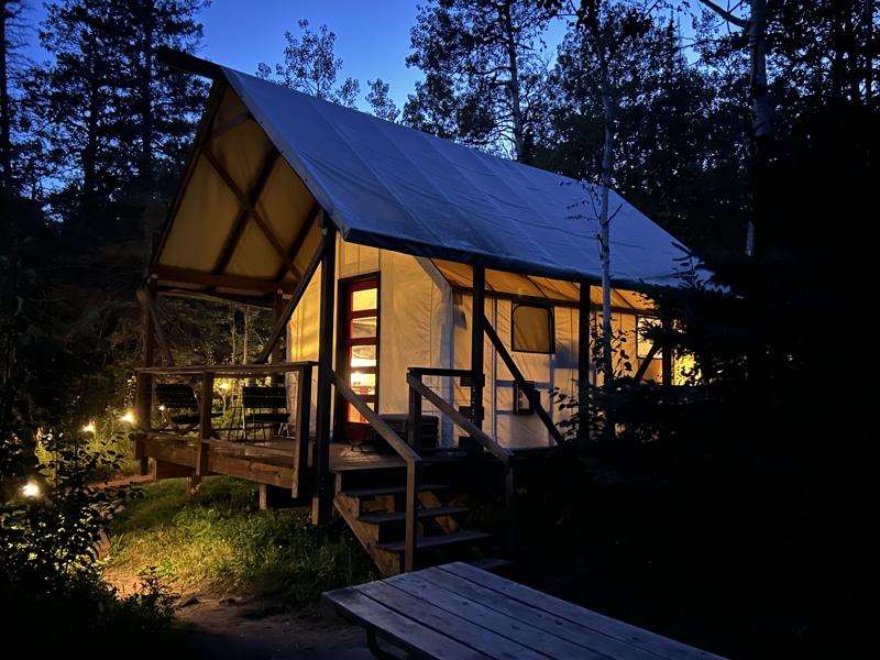 Cozy illuminated tent cabin at night in forest.