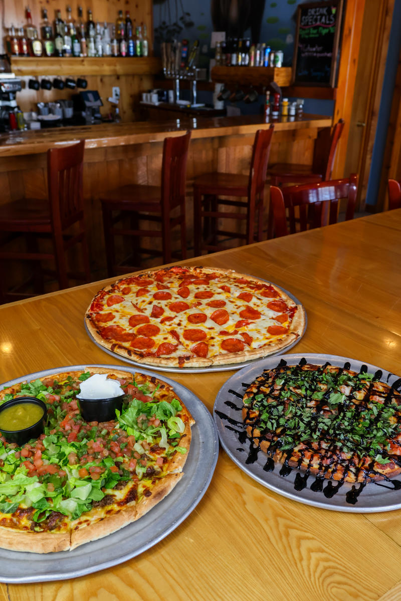 cove crossings food bev feb 2026 20 Three pizzas on a table in a cozy restaurant.