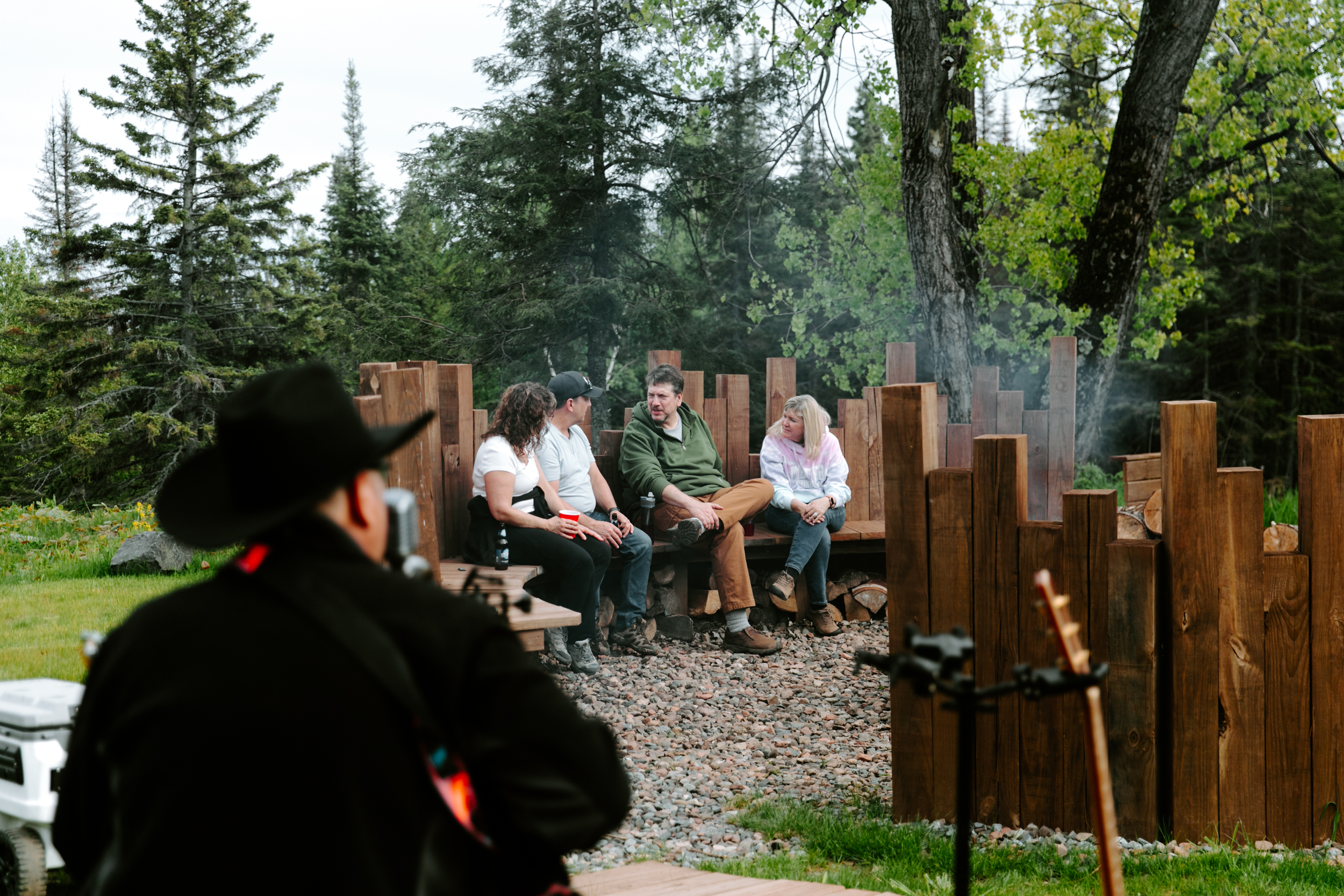 Group sitting by campfire with guitarist outdoors.