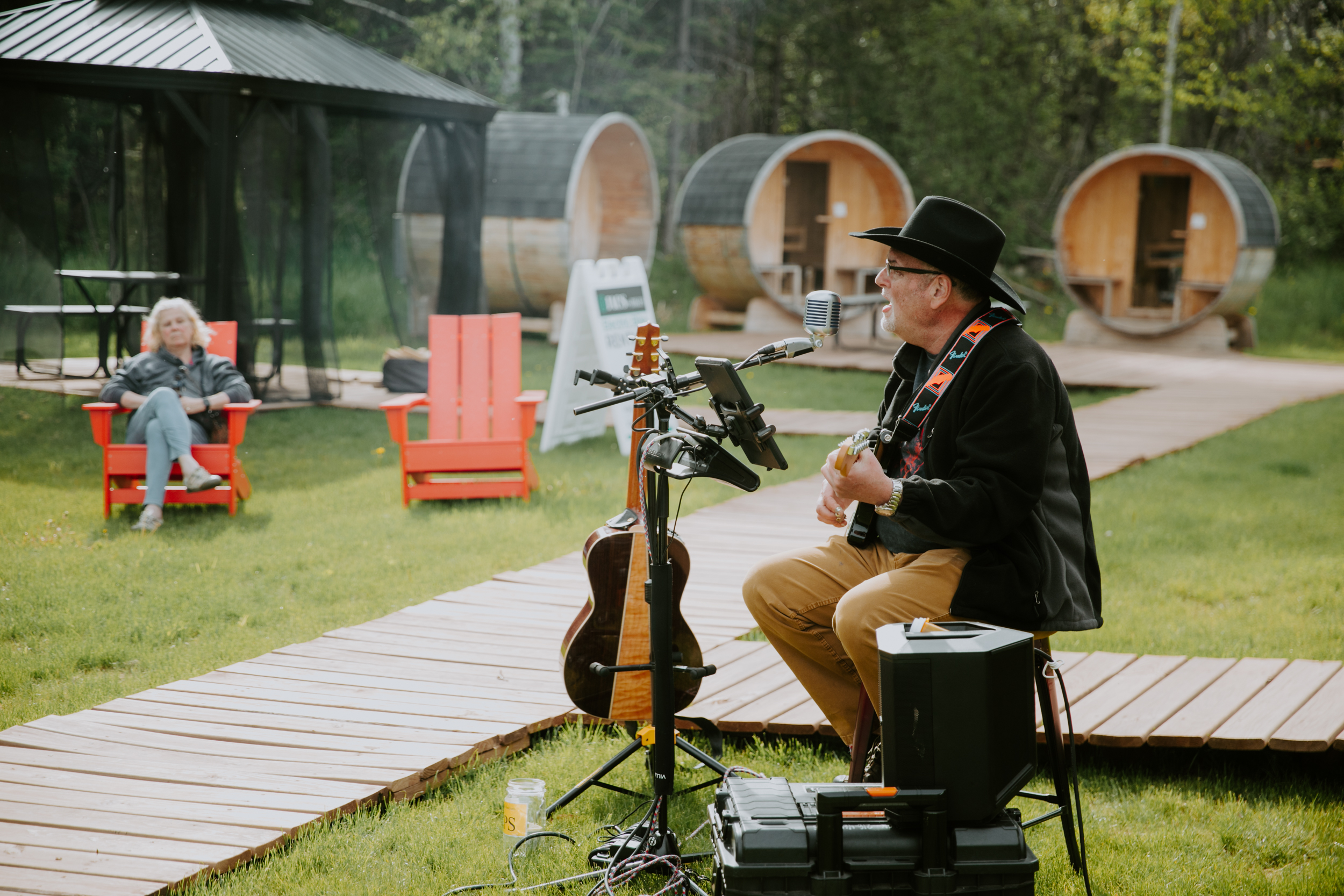 Man playing guitar outdoors with audience seated nearby.