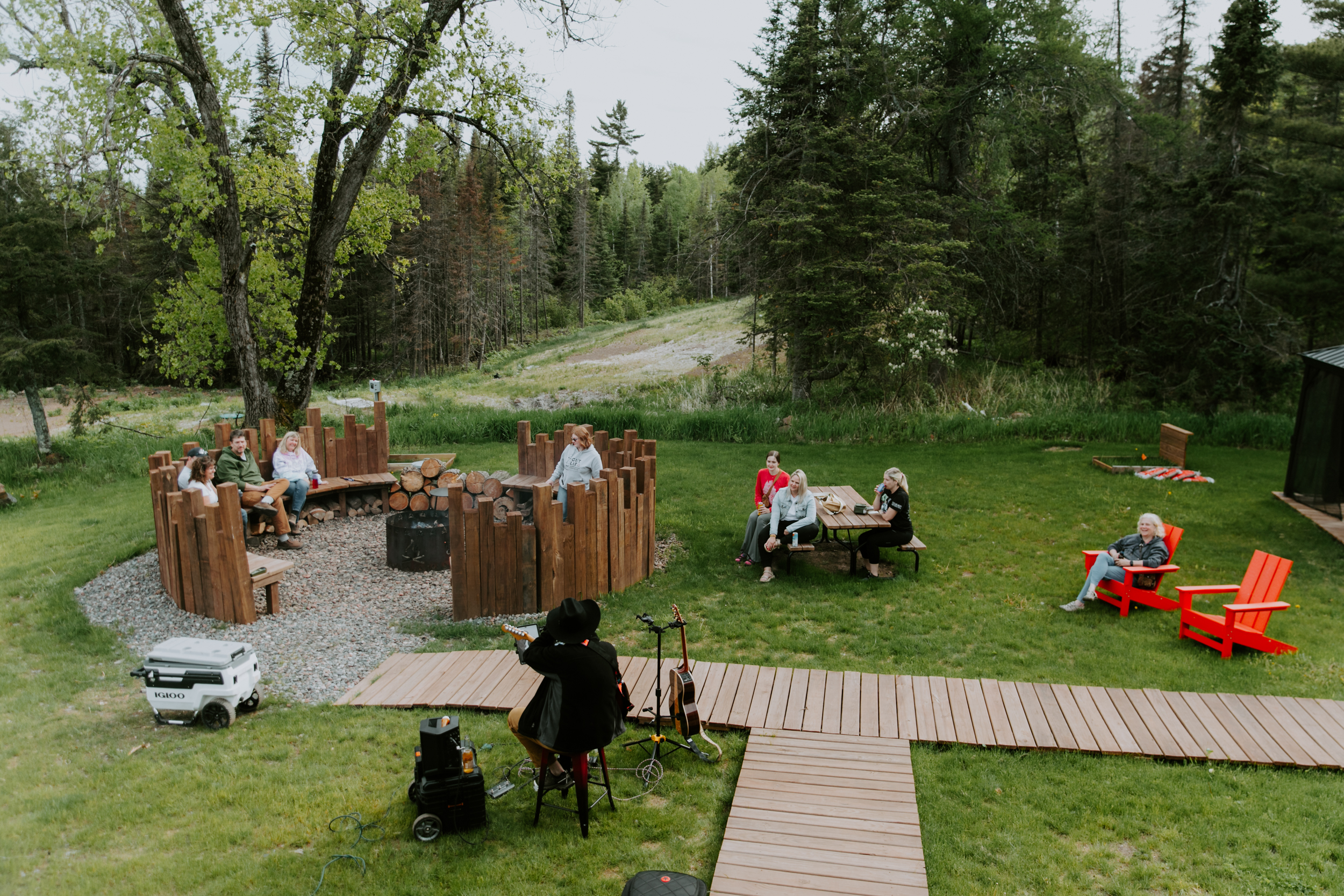 People relaxing around campfire in forest clearing.