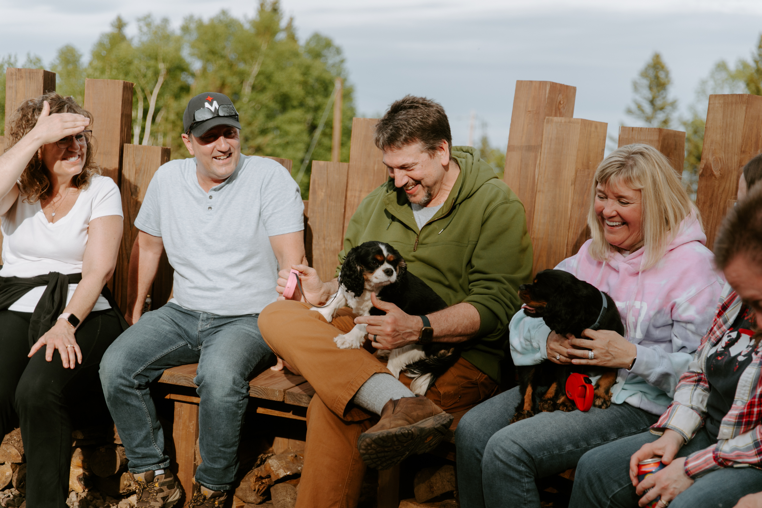 Group of people sitting with dogs outdoors.