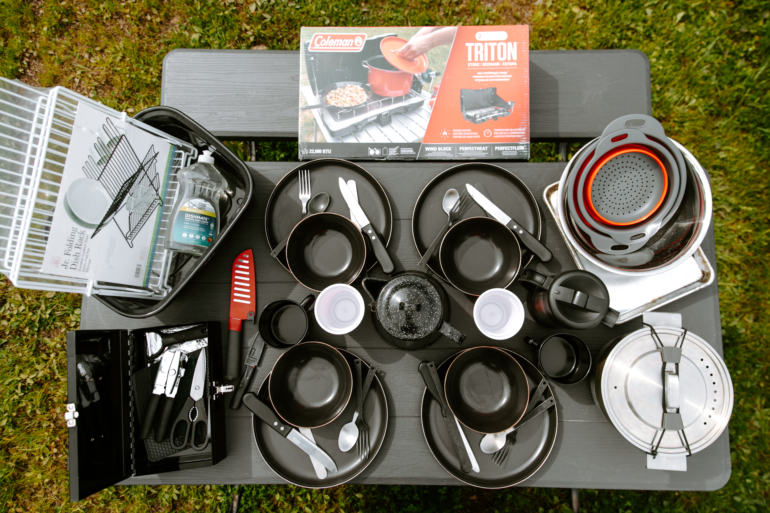 Camping cookware and accessories on a table outdoors.