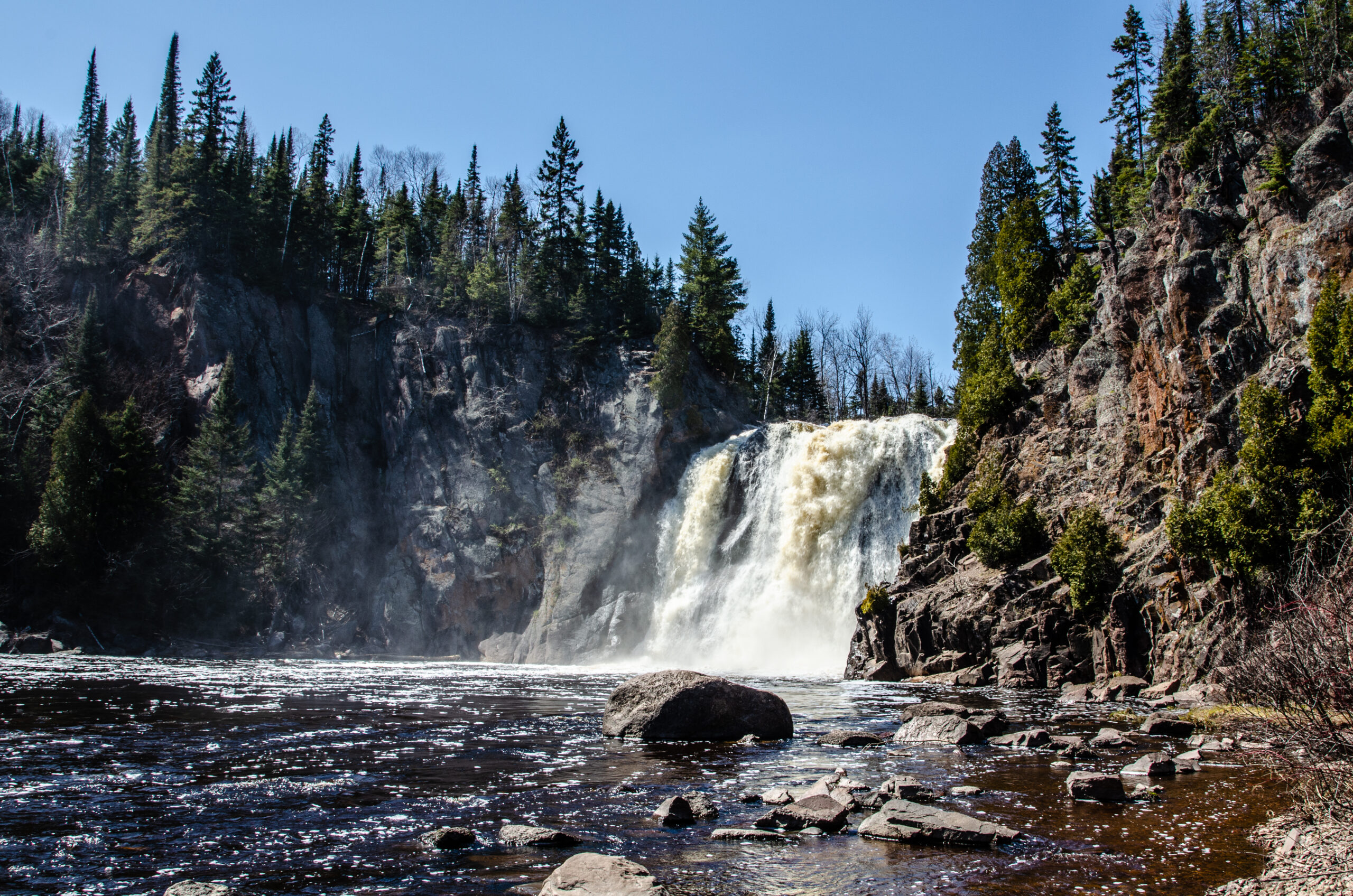 Scenic waterfall surrounded by forest and rocky cliffs.