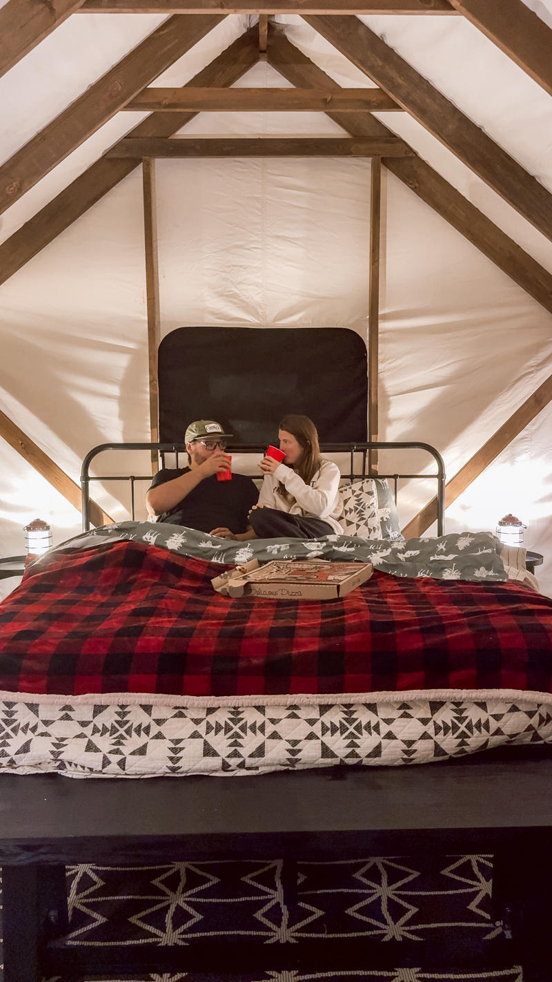 Couple relaxing with drinks in cozy cabin bed.