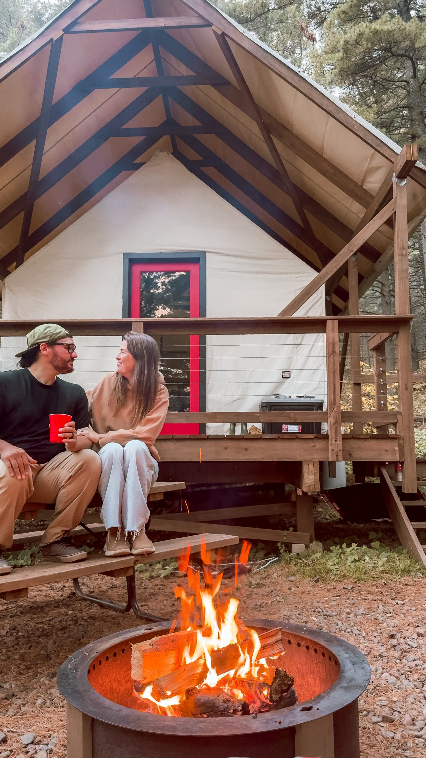 Couple sitting by campfire near cabin in woods.