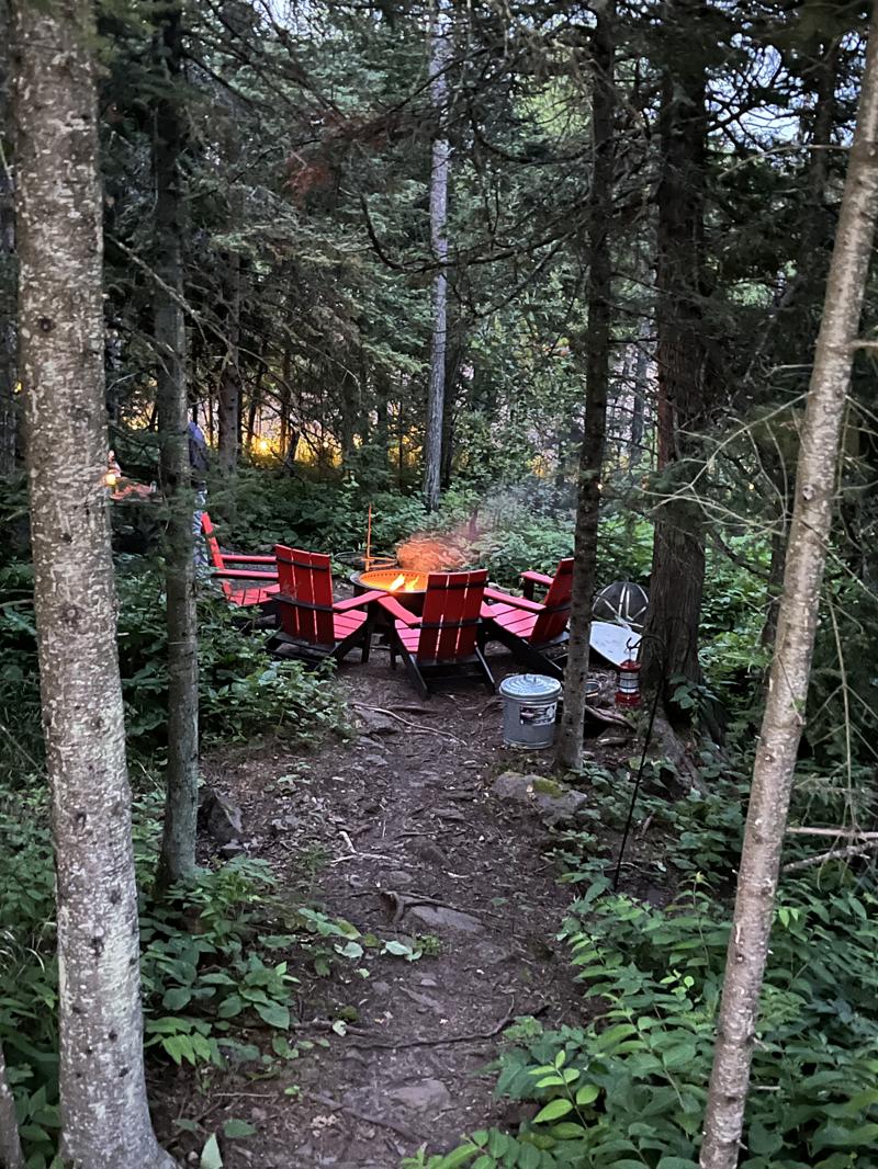 img 8393 Forest clearing with red chairs around fire pit.