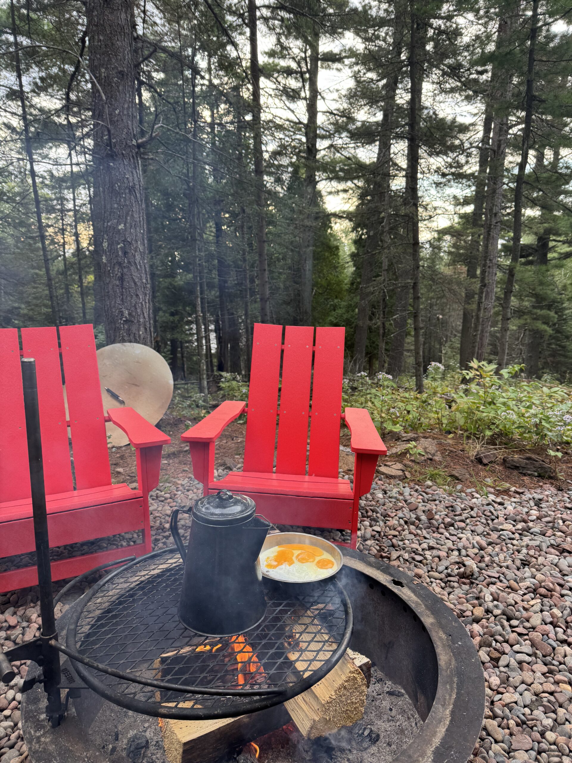 Campfire cooking with eggs, coffee, and red chairs.