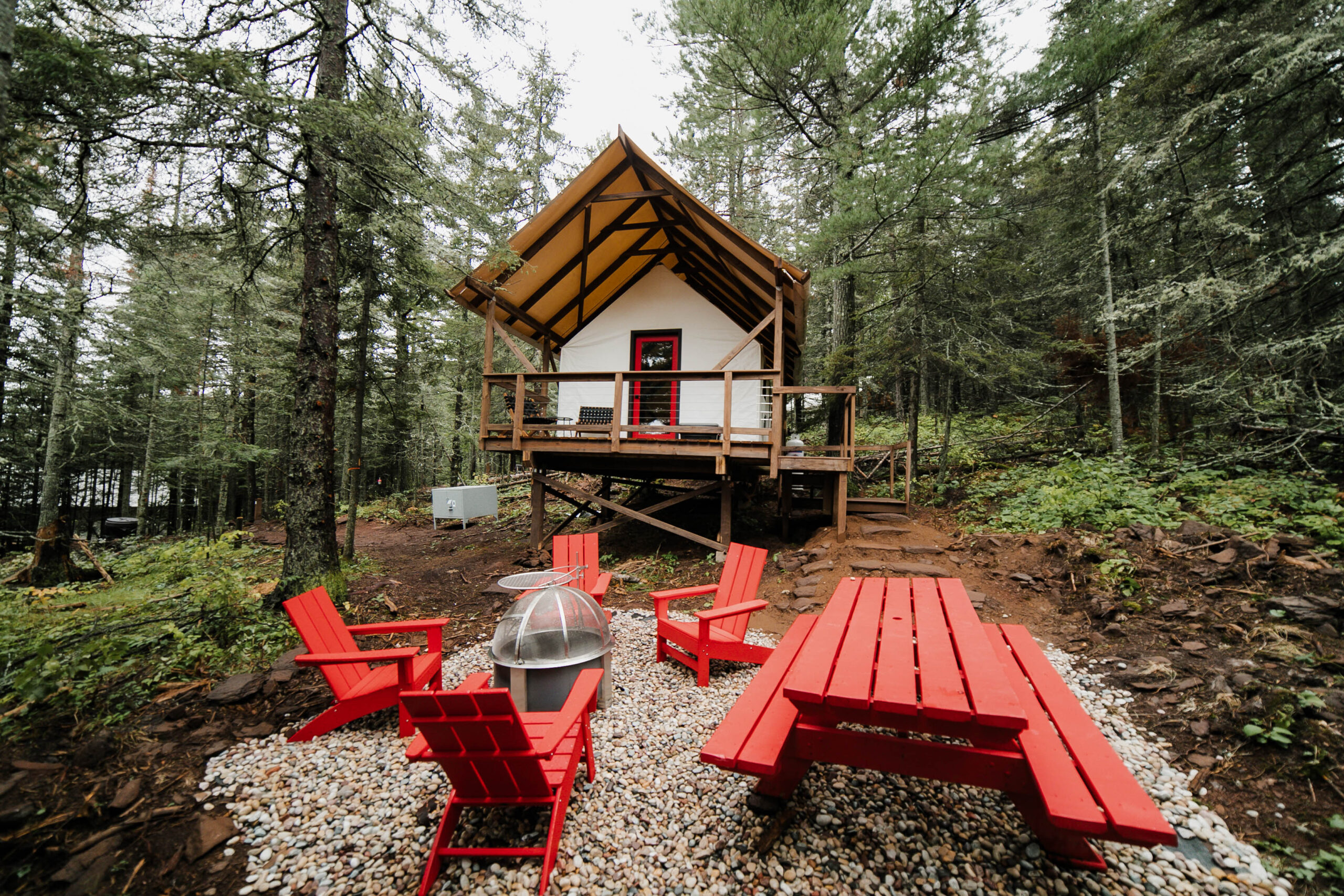 Rustic cabin with red chairs in forest setting.