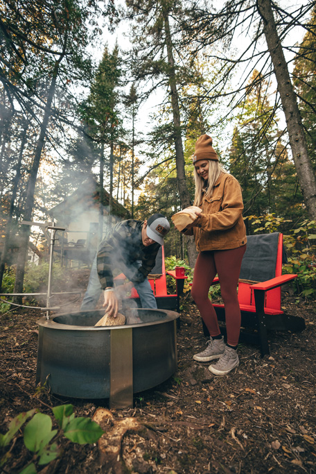 Couple lighting campfire in forest clearing.