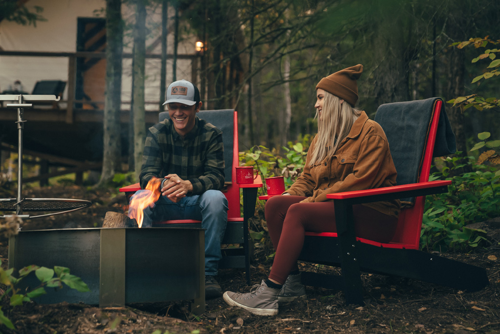 Couple sitting by campfire in forest setting.