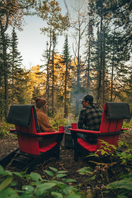 Two people sitting by campfire in forest.