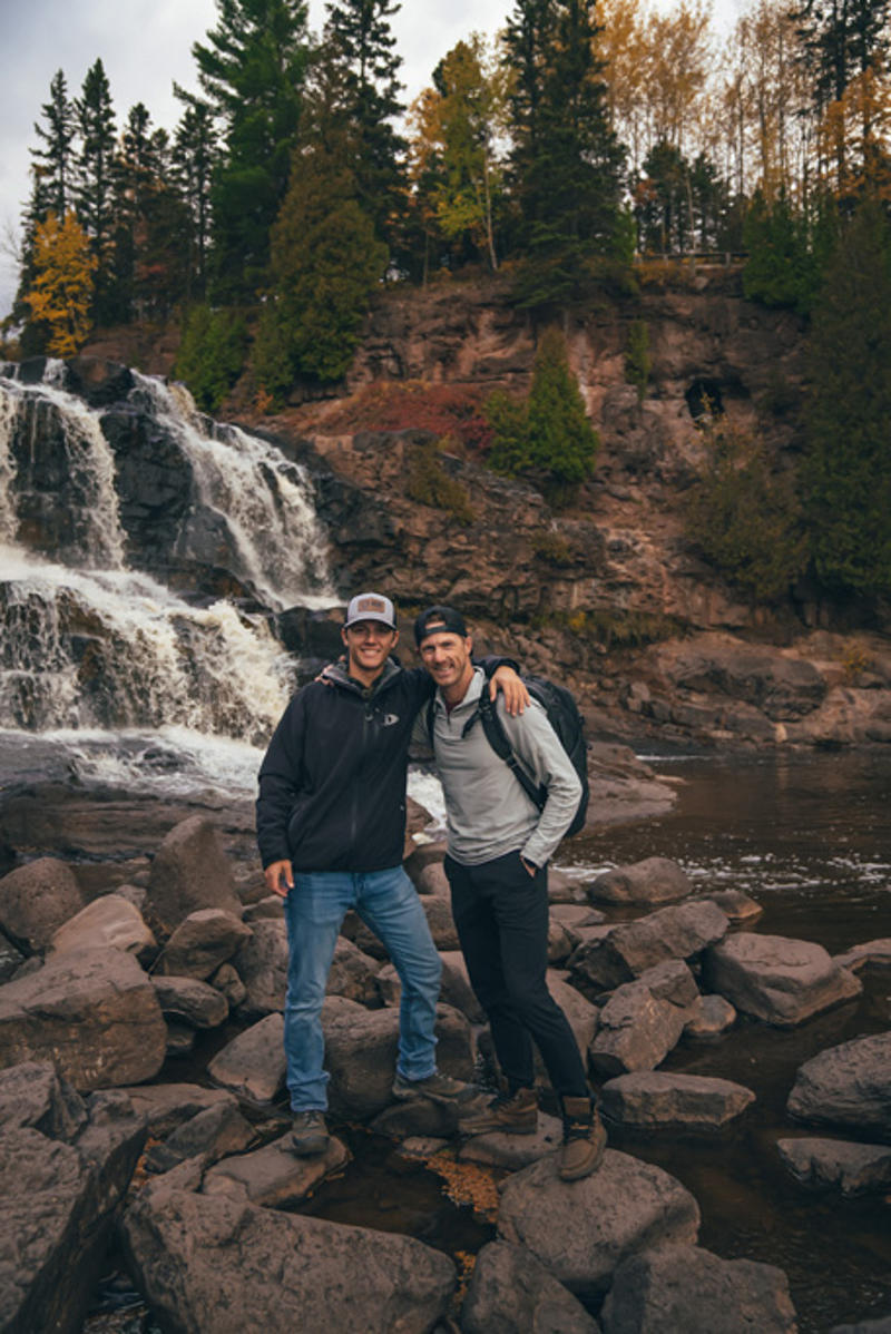 northshorecampingco fall2022 images 374 Two friends hiking near a waterfall and forest.