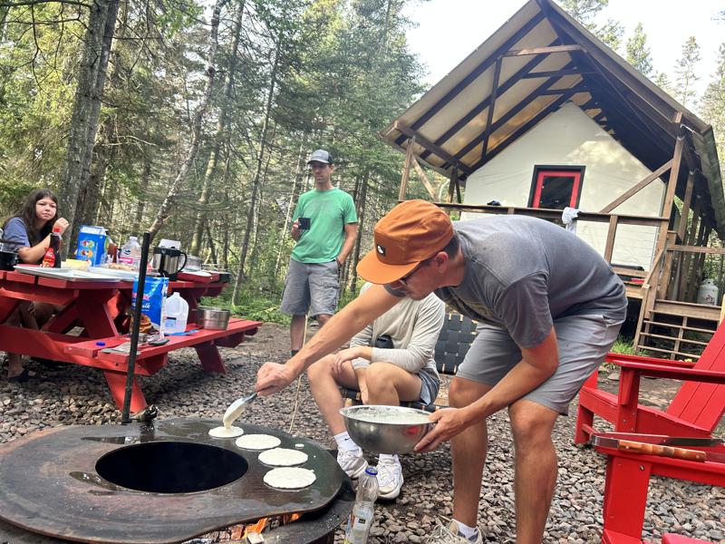 site 14 (2) Cooking pancakes outdoors near cabin and picnic tables.