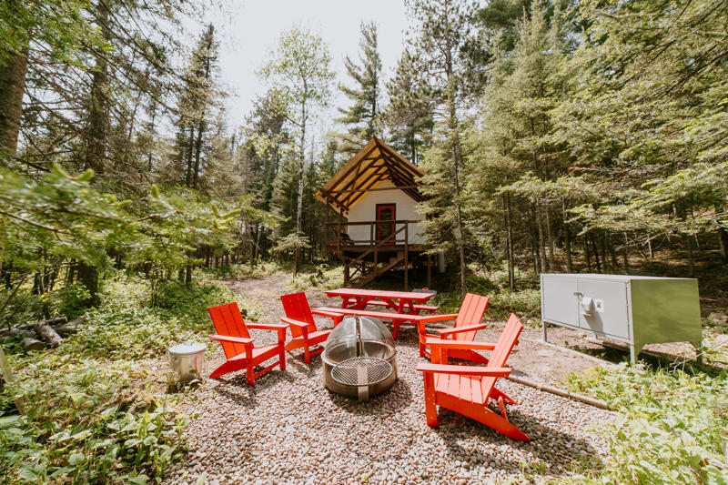 tent 17 (2) Cozy cabin with red chairs in forest setting.