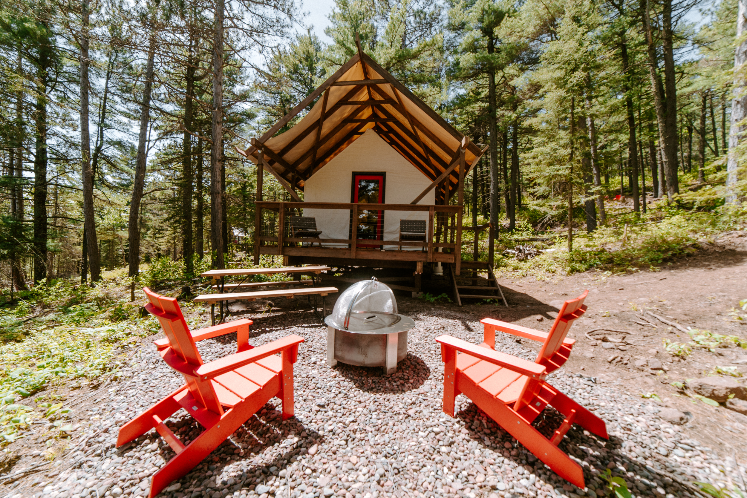Cabin with chairs and fire pit in forest.